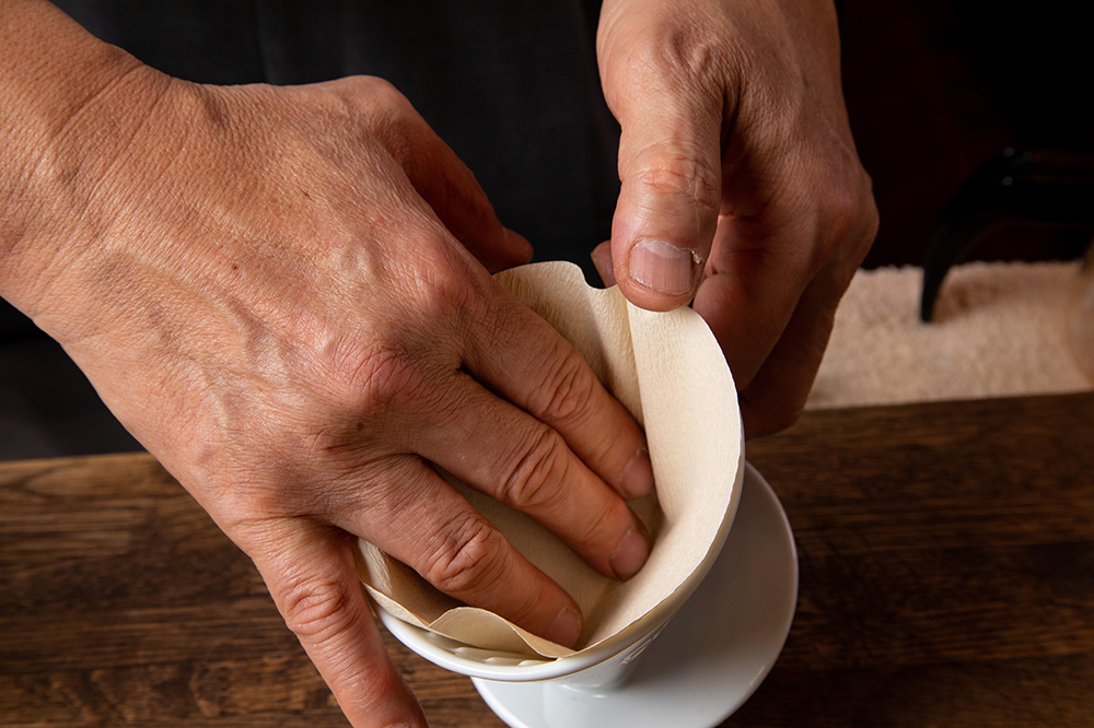 3.ろ紙を指でドリッパーに押し付け、密着させる。コーヒーの粉を入れ、表面を平らにする。